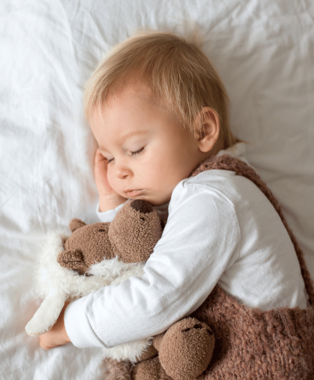 Sleeping toddler cuddling stuffed animals after bedtime